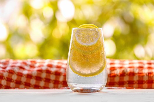 Glass of lemonade with lemon on the sunny garden background