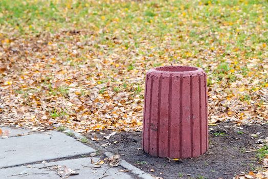 New red cement trash bin in the park in autumn