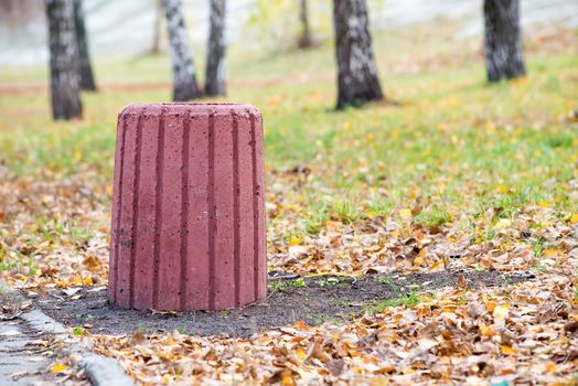 New red cement trash bin in the park in autumn