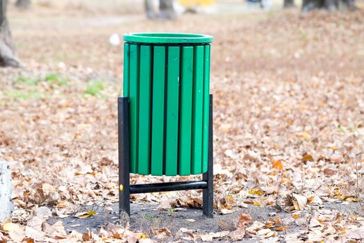 New green trash bin in the park in autumn