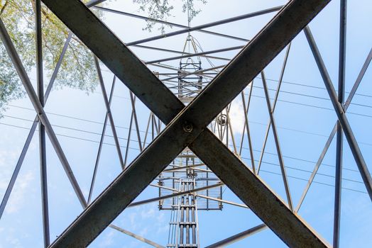 Detail of an electricity pylon against blue sky: high voltage electric cables seen from below