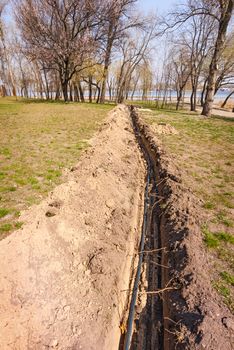 Installation of tubes for an irrigation system in the ground under the trees close to the river. Watering system in the Natalka park of Kiev, Ukraine
