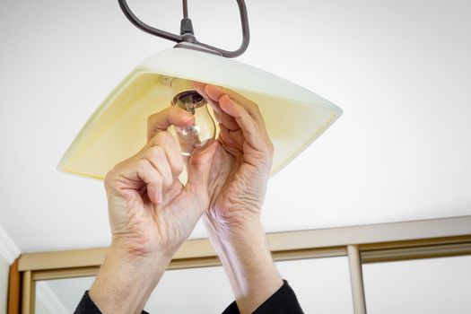 Man installing or changing a bulb, fixing it to the socket at home