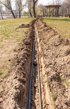 Installation of tubes for an irrigation system in the ground under the trees close to the river. Watering system in the Natalka park of Kiev, Ukraine