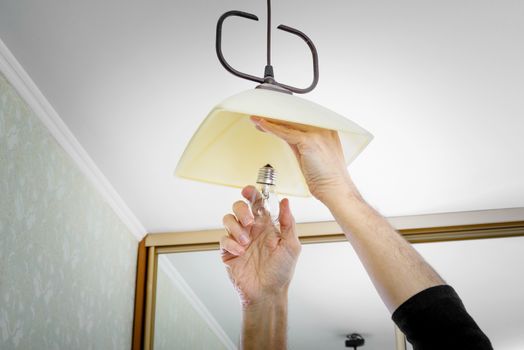 Man installing or changing a bulb, fixing it to the socket at home