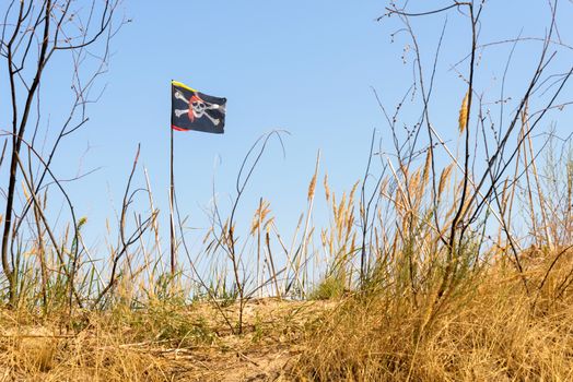 The black Jolly Roger pirate flag flutters in the wind over the hill