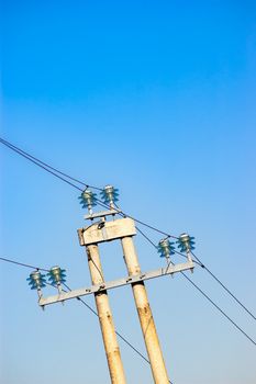 Electric power line with the wires set on isolators on a high pylon against clear blue sky