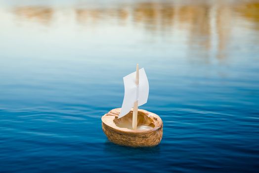 A walnut shell with a sail, floating on the blue lake
