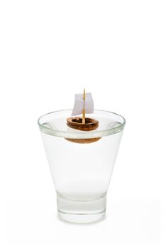 A walnut shell boat with a sail, floating in a transparent glass full of water or alcohol.