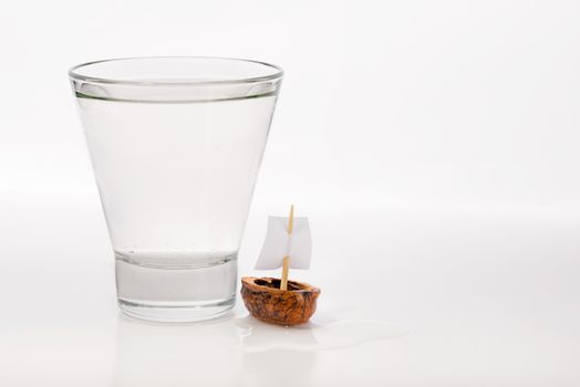 Closeup of a walnut shell boat with a sail, close to a transparent glass full of water or alcohol.