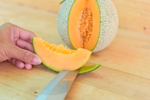 The man use knife split the orange melon on wood plate