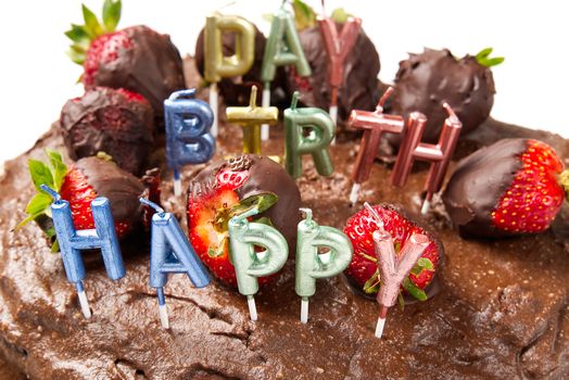 homemade chocolate cake with strawberries and happy birthday candles, close-up