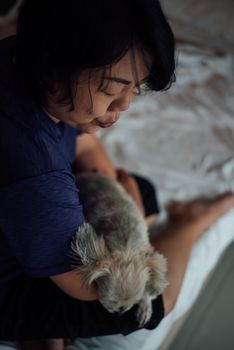 Asian woman and dog happy smile hugging her pat is a dog so cute mixed breed with Shih-Tzu, Pomeranian and Poodle on bed with white veil in bedroom at home or hotel