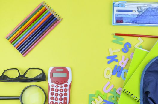 Student backpack and various school supplies. Studying, education and back to school concept. Yellow background and selective focus.