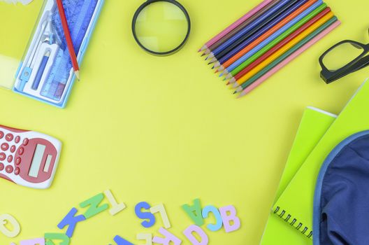 Student backpack and various school supplies. Studying, education and back to school concept. Yellow background and selective focus.