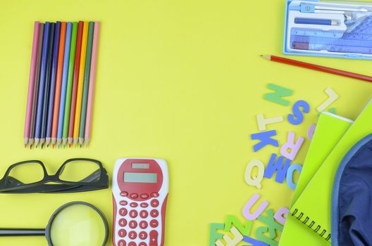 Student backpack and various school supplies. Studying, education and back to school concept. Yellow background and selective focus.