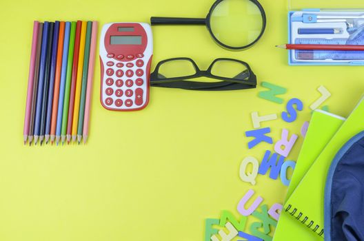 Student backpack and various school supplies. Studying, education and back to school concept. Yellow background and selective focus.