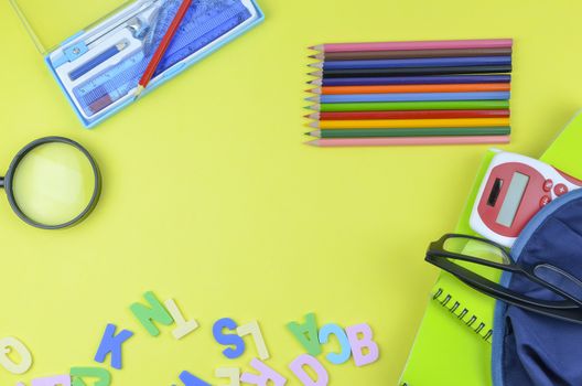 Student backpack and various school supplies. Studying, education and back to school concept. Yellow background and selective focus.