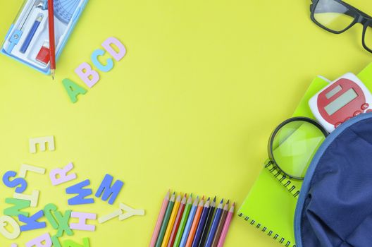 Student backpack and various school supplies. Studying, education and back to school concept. Yellow background and selective focus.