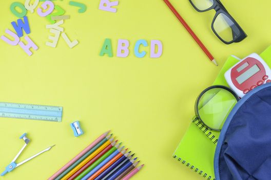 Student backpack and various school supplies. Studying, education and back to school concept. Yellow background and selective focus.