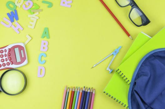 Student backpack and various school supplies. Studying, education and back to school concept. Yellow background and selective focus.