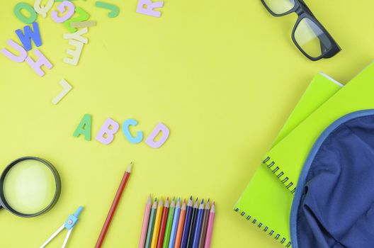 Student backpack and various school supplies. Studying, education and back to school concept. Yellow background and selective focus.