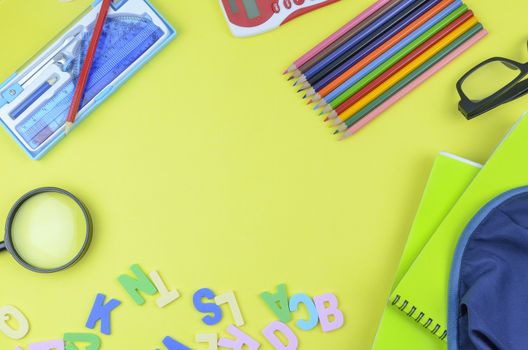 Student backpack and various school supplies. Studying, education and back to school concept. Yellow background and selective focus.