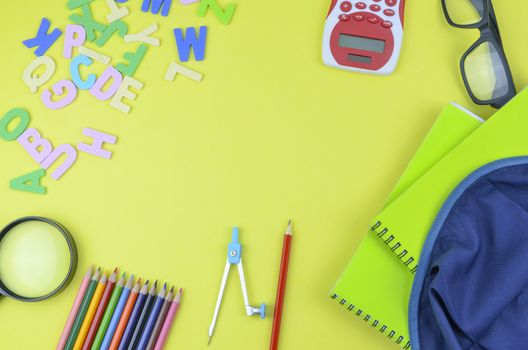 Student backpack and various school supplies. Studying, education and back to school concept. Yellow background and selective focus.