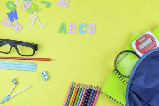 Student backpack and various school supplies. Studying, education and back to school concept. Yellow background and selective focus.