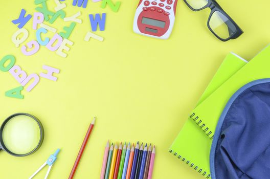 Student backpack and various school supplies. Studying, education and back to school concept. Yellow background and selective focus.