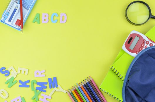 Student backpack and various school supplies. Studying, education and back to school concept. Yellow background and selective focus.