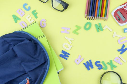 Student backpack and various school supplies. Studying, education and back to school concept. Yellow background and selective focus.