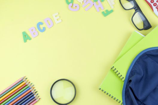 Student backpack and various school supplies. Studying, education and back to school concept. Yellow background and selective focus.