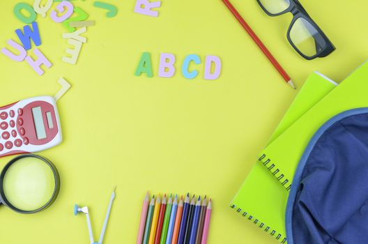 Student backpack and various school supplies. Studying, education and back to school concept. Yellow background and selective focus.