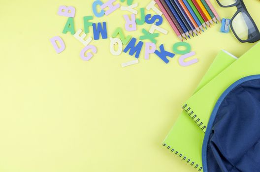 Student backpack and various school supplies. Studying, education and back to school concept. Yellow background and selective focus.