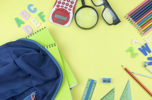 Student backpack and various school supplies. Studying, education and back to school concept. Yellow background and selective focus.