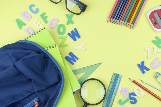 Student backpack and various school supplies. Studying, education and back to school concept. Yellow background and selective focus.