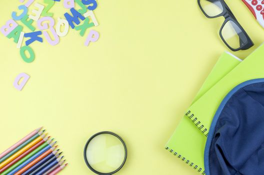 Student backpack and various school supplies. Studying, education and back to school concept. Yellow background and selective focus.