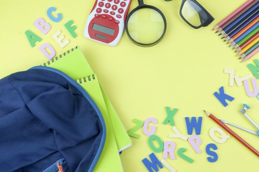 Student backpack and various school supplies. Studying, education and back to school concept. Yellow background and selective focus.