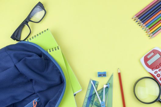 Student backpack and various school supplies. Studying, education and back to school concept. Yellow background and selective focus.