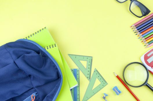 Student backpack and various school supplies. Studying, education and back to school concept. Yellow background and selective focus.