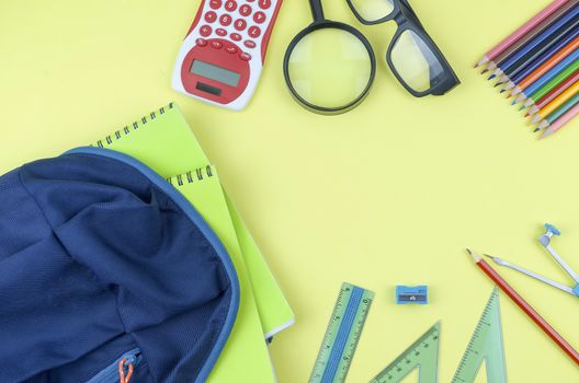 Student backpack and various school supplies. Studying, education and back to school concept. Yellow background and selective focus.