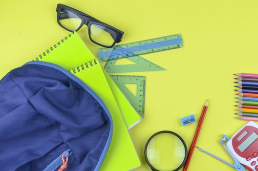 Student backpack and various school supplies. Studying, education and back to school concept. Yellow background and selective focus.