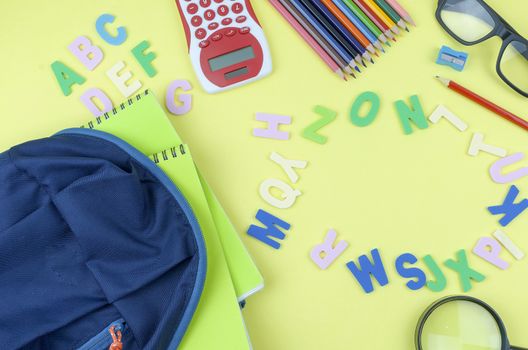 Student backpack and various school supplies. Studying, education and back to school concept. Yellow background and selective focus.