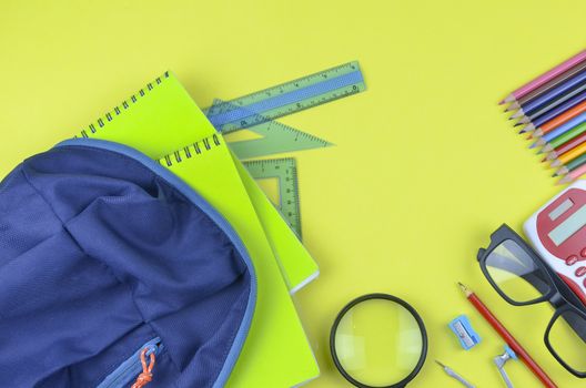 Student backpack and various school supplies. Studying, education and back to school concept. Yellow background and selective focus.