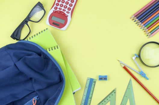 Student backpack and various school supplies. Studying, education and back to school concept. Yellow background and selective focus.