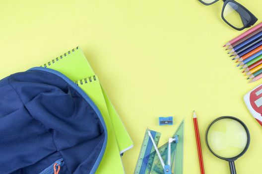 Student backpack and various school supplies. Studying, education and back to school concept. Yellow background and selective focus.