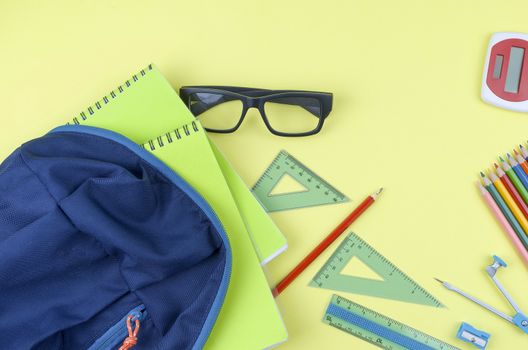 Student backpack and various school supplies. Studying, education and back to school concept. Yellow background and selective focus.