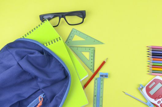 Student backpack and various school supplies. Studying, education and back to school concept. Yellow background and selective focus.