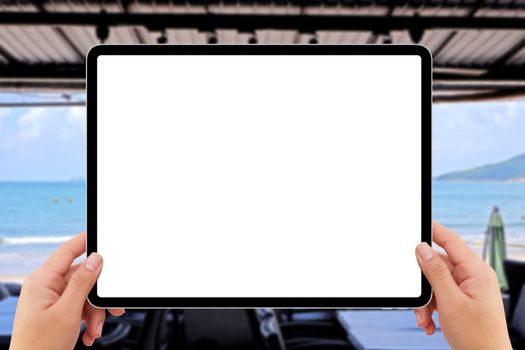 human two hands holding white tablet computer white screen mockup at indoor restaurant near beach
